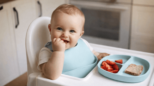 Baby sitting in a high chair eating fruit and bread